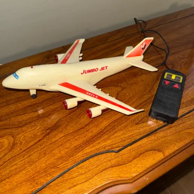 Sale Photo Thumbnail #321: Vintage plastic battery-operated Jumbo Jet toy airplane with tethered remote control, featuring red striping and S 328A decals.