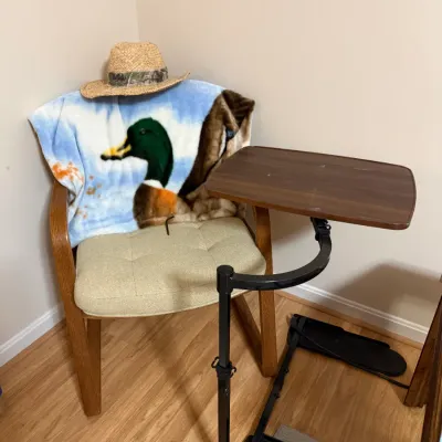 Sale Photo Thumbnail #374: Adjustable swivel tray table positioned in front of an upholstered wooden armchair decorated with a mallard duck fleece throw and a straw hat.