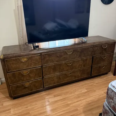 Sale Photo Thumbnail #109: Vintage Hollywood Regency style burl wood lowboy dresser with brass pulls, supporting a modern flat-screen television.