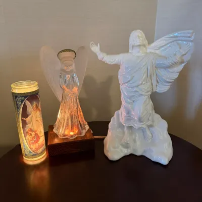 Sale Photo Thumbnail #229: Collection of religious decor items including a white ceramic statue of Jesus, an illuminated frosted glass angel on a wooden base, and a tall glass devotional candle.