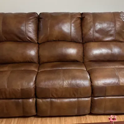 Sale Photo Thumbnail #6: Brown leather reclining sofa featuring nailhead trim detailing along rolled armrests and padded back cushions.