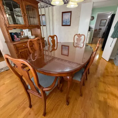 Sale Photo Thumbnail #221: Traditional wooden dining set featuring an oval glass-top table, six upholstered chairs, and a matching oak hutch in the background.