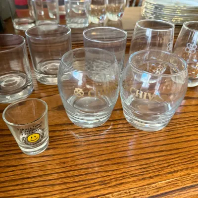 Sale Photo Thumbnail #315: Collection of assorted glassware, including Chivas branded whiskey glasses, plain lowball tumblers, and a smiley face novelty shot glass.