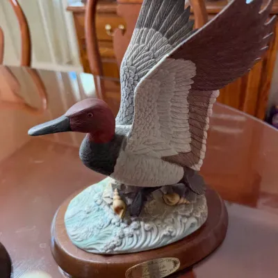 Sale Photo Thumbnail #281: Boehm porcelain canvasback duck figurine depicting wings outstretched over a water and seashell base, mounted on an oval wooden plinth.