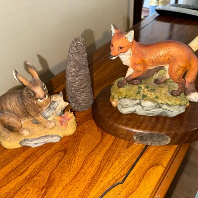 Sale Photo Thumbnail #275: Collection of three nature-themed porcelain and ceramic figurines, featuring a red fox mounted on a wooden base, a brown rabbit, and a pinecone decorative accent.