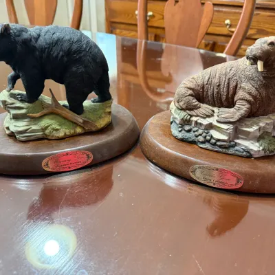Sale Photo Thumbnail #250: Pair of wildlife figurines featuring a black bear and a walrus, each mounted on a polished wooden base with a nameplate.
