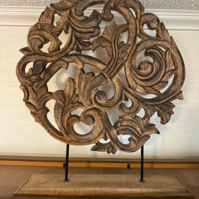 Sale Photo Thumbnail #225: Hand-carved wooden medallion featuring intricate scrollwork and acanthus leaf motifs, displayed on a dual-prong black metal stand with a matching wooden base.