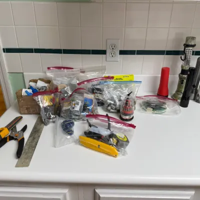 Sale Photo Thumbnail #163: Assorted collection of household tools, hardware in plastic bags, and flashlights arranged on a white countertop.