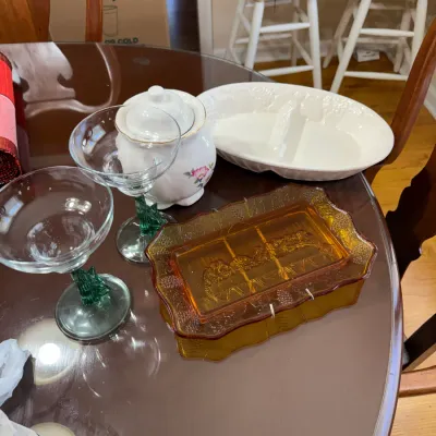 Sale Photo Thumbnail #197: Vintage glass tabletop items including an amber pressed glass Last Supper tray, green cactus-stem cocktail glasses, a floral ceramic jar, and a white oval serving dish.