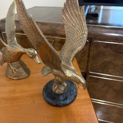 Sale Photo Thumbnail #362: Vintage brass eagle sculpture with outstretched wings mounted on a round stone base, shown alongside a brass duck figure.