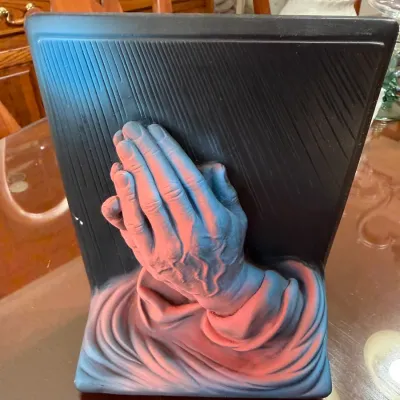 Sale Photo Thumbnail #192: Vintage ceramic praying hands plaque featuring a high-relief design with a textured dark background and dramatic pink highlights.