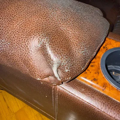 Sale Photo Thumbnail #71: Detail view of wear and peeling on a brown faux leather armchair armrest with a built-in cup holder.