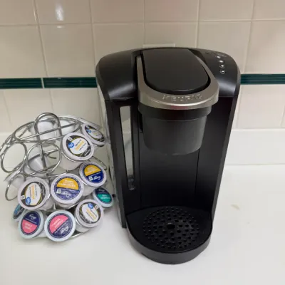 Sale Photo Thumbnail #149: Black Keurig single-serve coffee maker paired with a wire carousel pod holder containing various K-Cup pods.