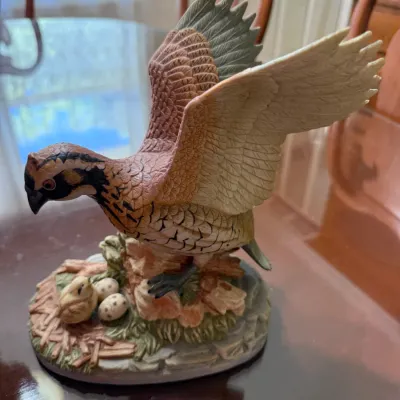 Sale Photo Thumbnail #254: Hand-painted porcelain bird figurine depicting a bobwhite quail with raised wings, perched above a nest with a chick and eggs.