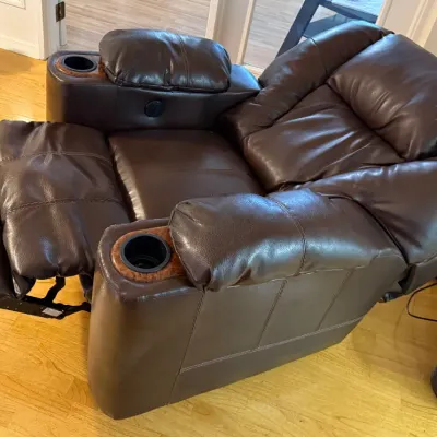 Sale Photo Thumbnail #73: Contemporary dark brown faux leather power recliner with built-in cup holders and padded armrests.
