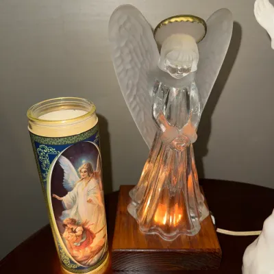 Sale Photo Thumbnail #232: Illuminated frosted glass angel figurine on a wooden base, displayed alongside a tall Guardian Angel devotional pillar candle.
