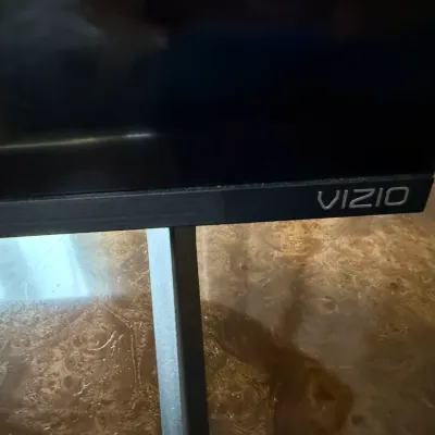Sale Photo Thumbnail #98: Close-up detail of a modern Vizio flat-screen television showing the brand logo on the lower bezel.