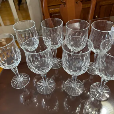 Sale Photo Thumbnail #310: Set of eight clear cut crystal wine glasses featuring a diamond pattern and starburst bases, presented on a polished wooden table.