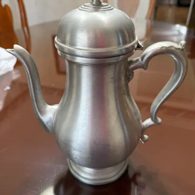 Sale Photo Thumbnail #203: Vintage pewter coffee pot featuring a domed lid with a urn finial, curved spout, and scroll handle.