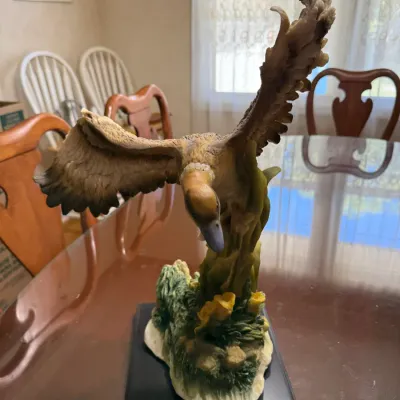 Sale Photo Thumbnail #260: Hand-painted resin bird figurine depicting a goose in flight over foliage, mounted on a black wooden base.