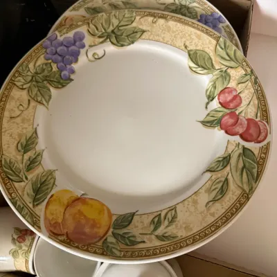 Sale Photo Thumbnail #295: Set of ceramic dinnerware featuring a Tuscan-style fruit border with painted grapes, cherries, and peaches, accompanied by matching mugs and a covered dish.