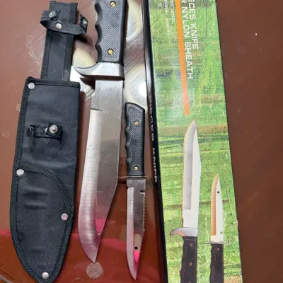 Sale Photo Thumbnail #268: Two-piece stainless steel hunting knife set with synthetic handles, including a large bowie-style knife, a smaller utility knife, a black nylon sheath, and the original packaging.