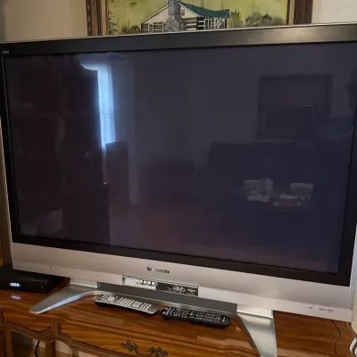 Sale Photo Thumbnail #91: Large Panasonic Viera flat-screen television with a silver bezel, silver table stand, and two remote controls.