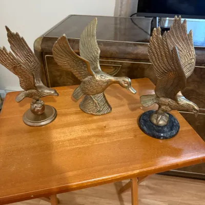 Sale Photo Thumbnail #361: Trio of vintage brass bird figurines featuring two eagles and a duck, displayed on a wooden folding table.