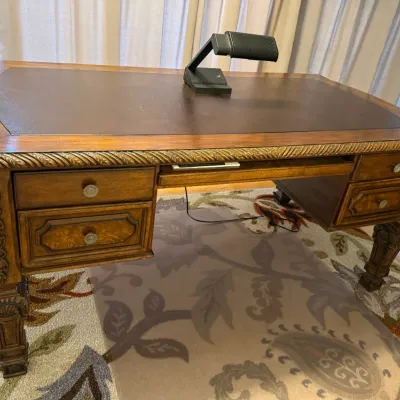 Sale Photo Thumbnail #55: Traditional wooden executive partner desk featuring a leather-inset top, carved rope edging, ornate leg details, and multiple drawers, topped with a modern desk lamp.