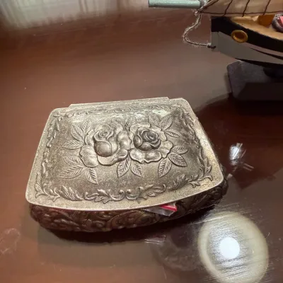 Sale Photo Thumbnail #259: Vintage embossed silver-tone trinket box featuring a detailed rose motif on the lid and floral scrollwork along the sides.