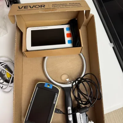 Sale Photo Thumbnail #155: Collection of low-vision aid devices including a Pebble HD electronic magnifier with charger, a VEVOR portable digital magnifier in box, and a handheld magnifying glass with light.