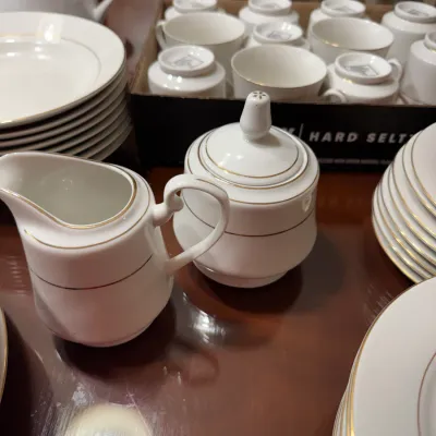 Sale Photo Thumbnail #306: White porcelain cream and sugar set with gold trim, shown alongside matching china dinnerware and teacups.