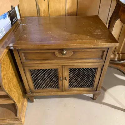 Sale Photo Thumbnail #388: Vintage wooden nightstand featuring a single upper drawer over lower cabinet doors with metal mesh panels. Shows moderate surface wear and finish distress on top.