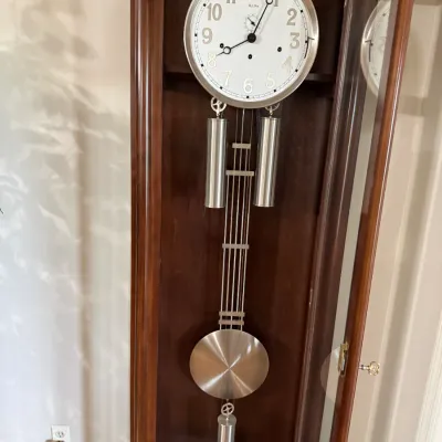 Sale Photo Thumbnail #3: Bulova grandfather clock featuring a dark wood cabinet, brushed silver face, cylindrical weights, and a gridiron pendulum.