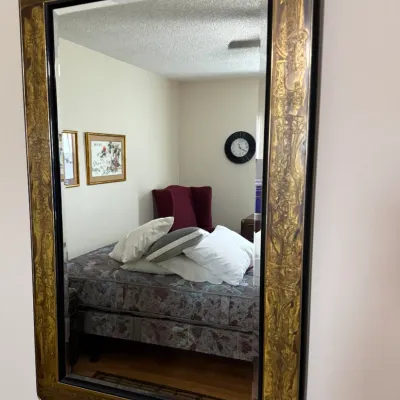 Sale Photo Thumbnail #101: Large rectangular wall mirror featuring an ornate gold-tone etched frame with black accents, reflecting a bedroom interior.