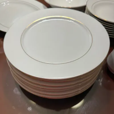 Sale Photo Thumbnail #300: Stack of white china dinner plates with gold rim accents, shown alongside matching bowls and serveware.
