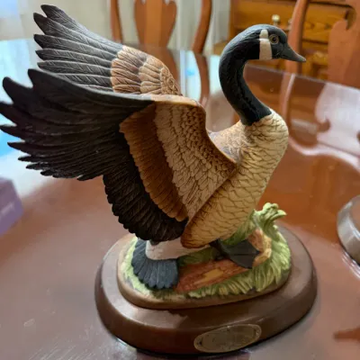 Sale Photo Thumbnail #279: Hand-painted porcelain Canada goose figurine with wings outstretched, mounted on a polished oval wooden base with a metal nameplate.