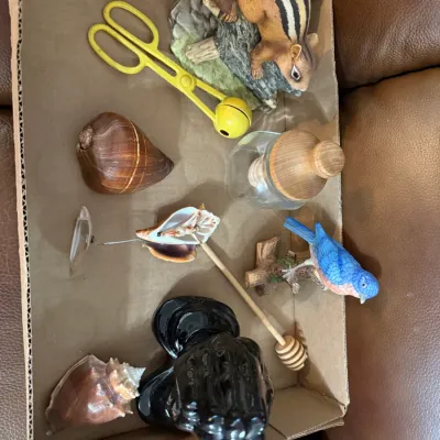 Sale Photo Thumbnail #345: Cardboard box containing a variety of small household items and collectibles, including bird and chipmunk figurines, seashells, a glass jar, and a wooden honey dipper.