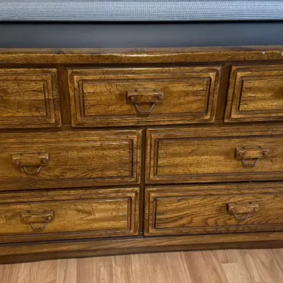 Sale Photo Thumbnail #115: Rustic distressed-finish wood dresser featuring seven drawers with unique wooden and metal bail handles and a dark top surface.