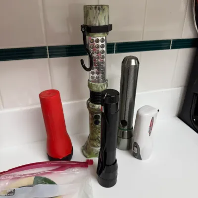 Sale Photo Thumbnail #165: Assorted collection of portable flashlights, including a camouflage hanging LED work light, a red plastic torch, metal tactical flashlights, and a hand-crank rechargeable model.