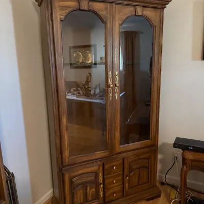 Sale Photo Thumbnail #226: Traditional oak display cabinet featuring arched glass-front upper doors, three central drawers, and lower storage cabinets with brass hardware.