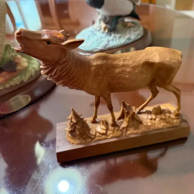 Sale Photo Thumbnail #280: Hand-carved wooden elk figurine displayed on a wooden base with scenic wilderness detailing, accompanied by waterfowl sculptures in the background.