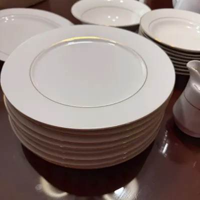 Sale Photo Thumbnail #302: Stack of white porcelain dinner plates with gold rim trim, accompanied by matching bowls and serving pieces.