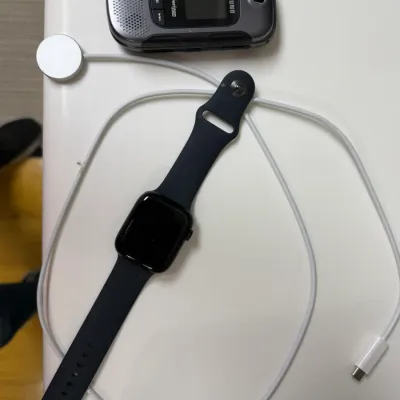 Sale Photo Thumbnail #162: Black smartwatch with a dark silicone band and magnetic charging cable, shown alongside a vintage Samsung Verizon flip phone.