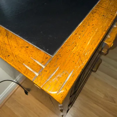 Sale Photo Thumbnail #117: Vintage executive desk featuring a black inlay top surrounded by a distressed orange and black speckled wood border.