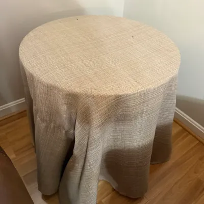 Sale Photo Thumbnail #338: Round accent table covered with a neutral beige woven fabric tablecloth, standing in a room corner.