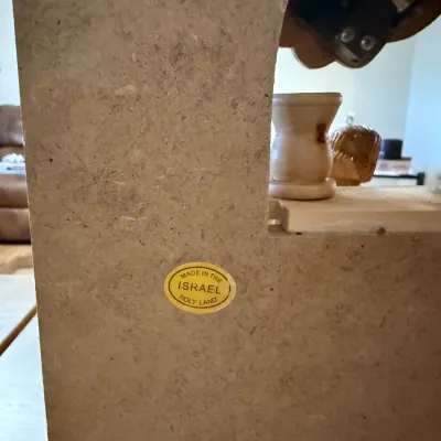 Sale Photo Thumbnail #160: Close-up of a particleboard wooden item featuring an original oval sticker that reads "Made in the Israel Holy Land".