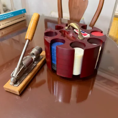 Sale Photo Thumbnail #195: Vintage wooden carousel poker chip caddy loaded with chips and playing cards, shown alongside a tabletop metal pecan cracker on a wooden base.