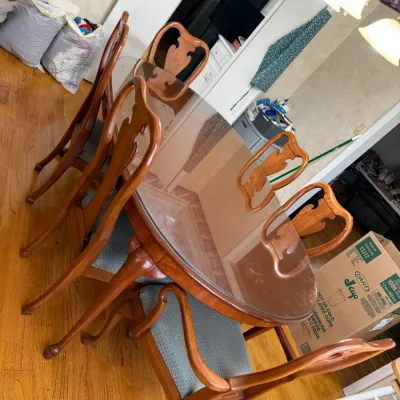Sale Photo Thumbnail #220: Queen Anne style wooden dining table with a protective glass top set, accompanied by six matching carved dining chairs with upholstered seats.