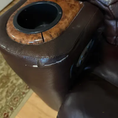 Sale Photo Thumbnail #121: Brown leather recliner armrest with built-in cupholder, showing a crack in the faux-wood trim and visible wear along the leather seam.